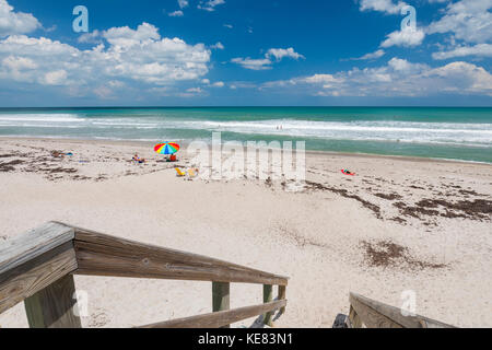 Les baigneurs de soleil s'assoient sur le sable de Pelican Beach avec un parasol coloré donnant sur l'océan Atlantique, et des marches en bois avec balustrade dans le front... Banque D'Images