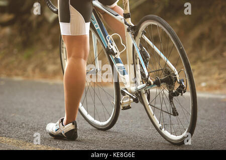 Un gros plan sur les pieds d'un cycliste féminine assise sur son vélo de route pendant le coucher du soleil  Banque D'Images