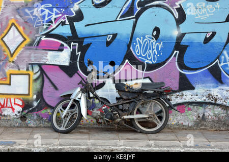 Un vieux et fatigués du cyclomoteur ou moto garée cycle contre un mur recouvert de graffitis à corcyre. Corfou sur une île grecque. art graphique, artiste de rue Banque D'Images