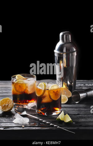 Composition au point sélective avec le Rhum et cola cocktail servis avec des agrumes sur du papier rugueux et fabrick sur la table en bois avec des morceaux de glace Banque D'Images