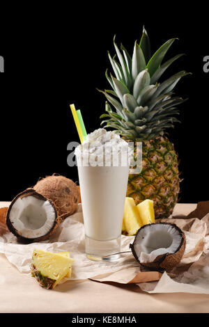 Composition au point sélective avec cocktail de noix de coco servi avec de l'ananas et noix de coco sur un papier sur la table en bois Banque D'Images