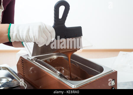 Un gros plan d'une femme dans un tablier blanc confiseur équivaut, à l'aide d'une spatule, chocolat chaud sur les tortues les tortues en forme de chocolat préparation. Banque D'Images