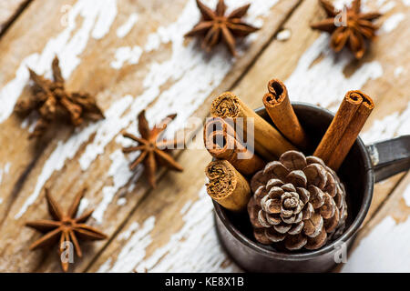 Décoration de Noël ingrédients dispersés bâtons de cannelle anis star pine cone dans vintage pot sur fond de bois enneigés carte de souhaits des fêtes. Banque D'Images