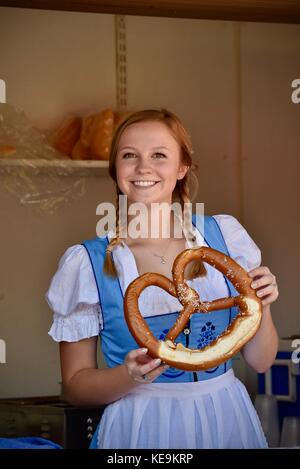 Belle jeune femme aux cheveux tressés en portant des dirdl traditionnelle suisse dress holding fresh grand bretzel à l'Oktoberfest à new glarus, Wisconsin, États-Unis Banque D'Images