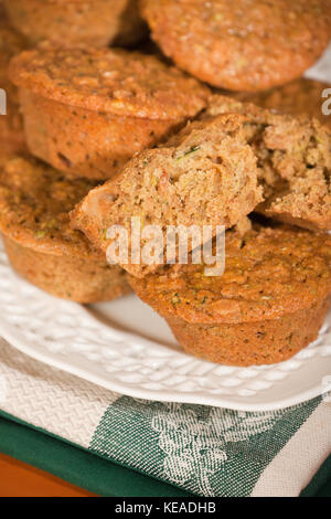 Muffins aux courgettes, avec une coupe dans la moitié, empilés sur une plaque en céramique blanche posée sur un plateau , sur une table en bois Banque D'Images