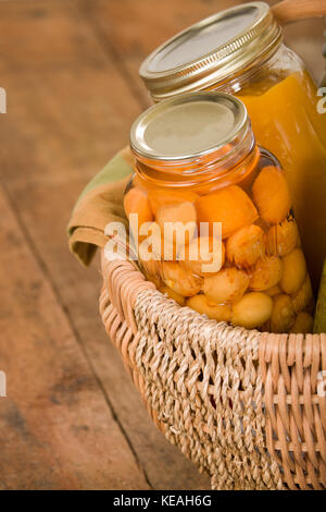 Accueil-produits en conserve (cerises Rainier et soupe à la courge musquée) dans un grand panier en osier posé sur une table en bois rustique Banque D'Images