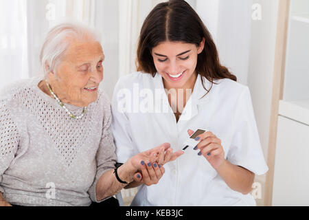 Professionnels féminins à contrôler le niveau de sucre dans le sang du patient avec des cadres supérieurs en clinique diabete Banque D'Images