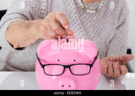 Close-up of Senior Woman's Hand Inserting Coin In Piggybank Banque D'Images