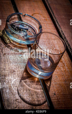 Cendrier en verre de whisky vide et avec des bâtons de cigarette sur cigarette. table en bois, de l'alcool. concept tumbler glass, cendrier, bâtons de cigarettes sur la table. Banque D'Images