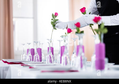 Close-up of waiter organiser roses dans vase sur la table de mariage Banque D'Images