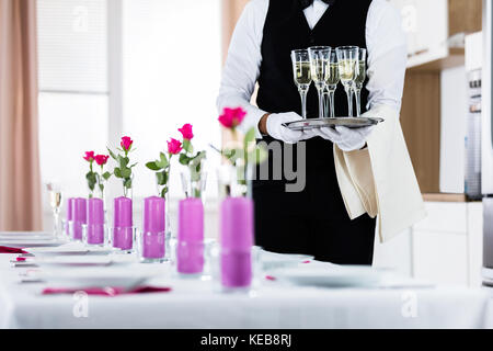 Waiter standing avec verres de champagne à côté de table de mariage arrangé Banque D'Images