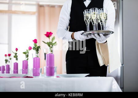 Waiter standing avec verres de champagne à côté de table de mariage arrangé Banque D'Images