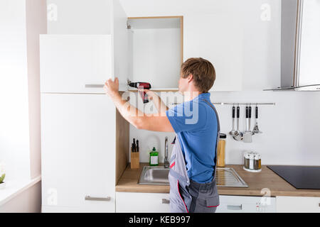 Male carpenter forage dans le cabinet avec perceuse électrique Banque D'Images