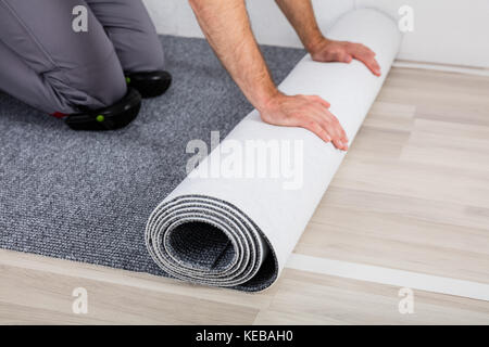 Close-up des mains du travailleur en déroulant le tapis sur le plancher à la maison Banque D'Images