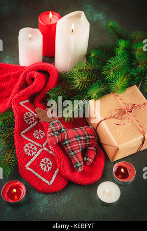 Noël et nouvel an arrière-plan avec des branches de sapin, cierge allumé, les noix et les épices, et les chaussettes rouges avec un jouet tissu deer et présente en kraft pap Banque D'Images