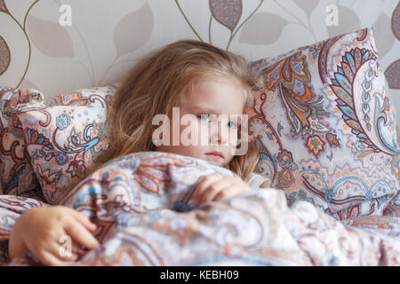 Une petite fille se trouve dans un triste lit. Banque D'Images