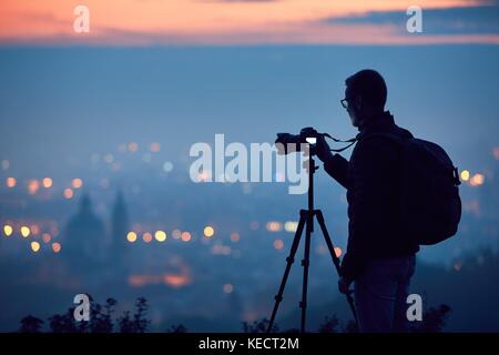 Silhouette de la photographe avec trépied. jeune homme de prendre des photos avec son appareil photo dans la nuit. La ville de Prague, République tchèque. Banque D'Images