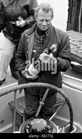 AJAXNETPHOTO. - 29ème mars, 1982. GOSPORT, ENGLAND. WHITBREAD - WORLD RACE - GAGNANT GLOBAL FLYER SKIPPER CORNELIS VAN RIETSCHOTEN ENVISAGE UNE BOUTEILLE DE CHAMPAGNE À bord du yacht de luxe à l'arrivée. PHOTO:JONATHAN EASTLAND/AJAX REF:822903418 Banque D'Images