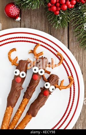 Le renne de noël fun bretzel au chocolat, les tiges au-dessus d'une plaque rouge et blanc Banque D'Images