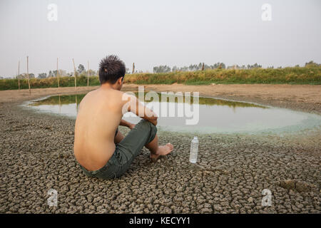 Crise de l'eau, l'homme s'asseoir sur la terre craquelée de séchage près de l'eau. Banque D'Images