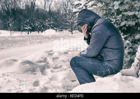 Homme assis sur un banc dans une forêt en hiver avec de la neige au sol Banque D'Images