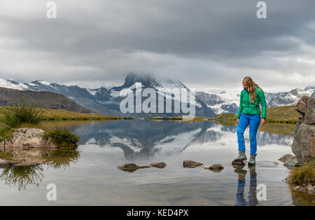 Randonneur marche sur des pierres dans l'eau, stellisee, couvertes de nuages Matterhorn, Valais, Suisse Banque D'Images
