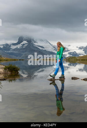 Randonneur marche sur des pierres dans l'eau, stellisee, couvertes de nuages Matterhorn, Valais, Suisse Banque D'Images