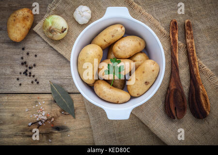Produits frais bio pommes de terre dans un bol en céramique blanche avec des ingrédients et des herbes , le persil, l'ail, les feuilles de laurier, le poivre, l'oignon et sel rose de l'himalaya sur le chanvre Banque D'Images