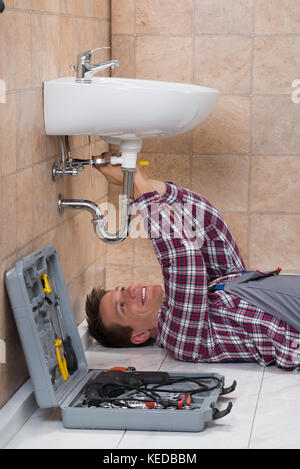 Heureux jeune homme de plombier dans la salle de bains lavabo Fixation Banque D'Images