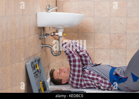 Heureux jeune homme de plombier dans la salle de bains lavabo Fixation Banque D'Images