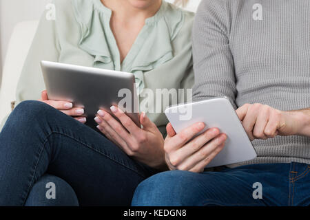Close-up of young couple with digital tablets sitting on sofa Banque D'Images