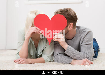 Couple derrière forme de coeur tout en se trouvant sur un tapis à la maison Banque D'Images