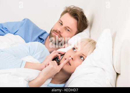Young man looking at Woman talking on mobile phone dans la chambre à la maison Banque D'Images