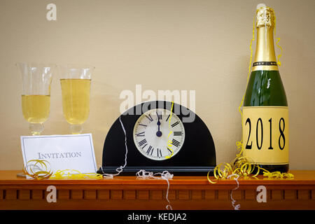 Une horloge indiquant minuit au nouvel an avec une bouteille de champagne étiqueté 2018, verres et invitation entouré de banderoles. Banque D'Images