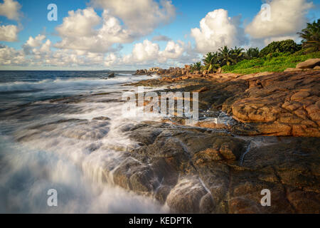 Vagues se briser contre les roches de granit rouge en face d'une jungle sauvage rugueux. - l'autre côté du paradis sur les seychelles. Banque D'Images