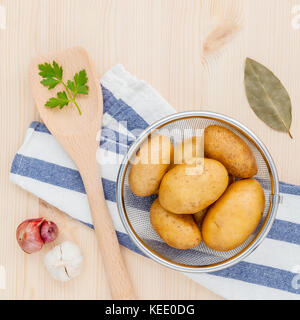 Des pommes de terre biologiques frais dans panier avec herbes ail échalote,,le persil et les feuilles de laurier sur table en bois rustique. préparation pour la cuisson. Banque D'Images