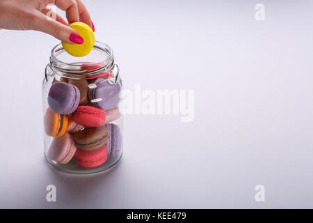 La prise de main de femme jaune délicieux macarons de pot de verre sur fond gris clair. Un espace réservé au texte Banque D'Images