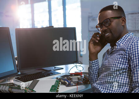 Ingénieur informatique talking on mobile phone at desk in office Banque D'Images