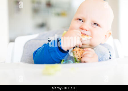 Baby Boy eating bread et concombre avec méthode, BLW led bébé sevrage. Heureux végétariens kid au dîner. Tout-petit manger lui-même, auto-alimentent. Banque D'Images