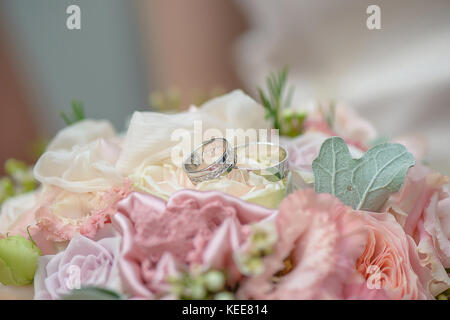 Close-up shot de pastel bouquet de roses et de soie avec deux anneaux de mariage reposant sur une rose blanche, prêt pour la cérémonie de mariage Banque D'Images