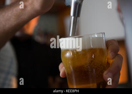 La mi-section de remplissage brasseur de la bière dans le verre de bière à partir de la bière au bar de la pompe Banque D'Images