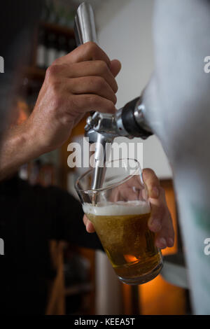 La mi-section de remplissage brasseur de la bière dans le verre de bière à partir de la bière au bar de la pompe Banque D'Images