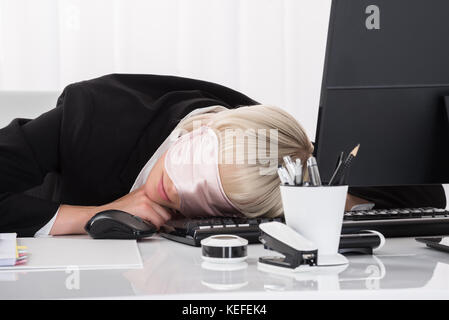 Young Businesswoman Wearing Eye Mask et dormir sur Desk In Office Banque D'Images