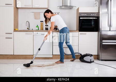 Jeune femme heureuse nettoyage du plancher de la cuisine à l'aide d'Aspirateur Banque D'Images