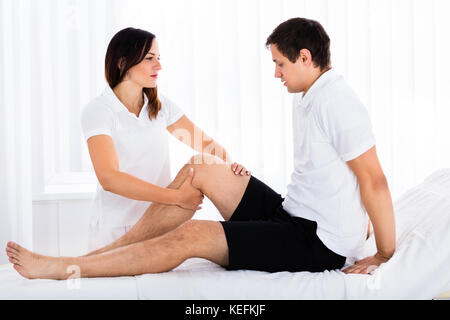 Photo de Female Therapist Massaging Young Man's Leg Banque D'Images
