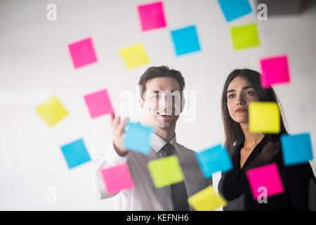 Démarrer la planification des activités et décisions de l'organisation jeune couple à l'intérieur de bureaux modernes à écrire des notes sur des autocollants Banque D'Images