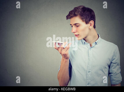 Jeune homme à l'aide d'un smart phone fonction reconnaissance vocale isolé sur fond de mur gris Banque D'Images