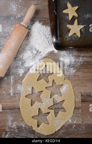 Vue de dessus de la pâte à biscuits avec star formes et de l'emporte-pièce sur la table de bois avec un rouleau à pâtisserie et saupoudrer de farine et de biscuits. Banque D'Images