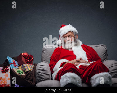 Sleepy santa claus prendre une sieste et reposant sur le fauteuil la veille de Noël Banque D'Images