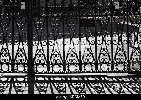 Porte en fer forgé avec des bars et des ombres sur le trottoir Banque D'Images